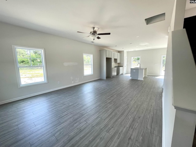 unfurnished living room with ceiling fan, dark wood-style flooring, and baseboards