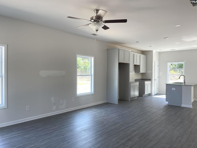 unfurnished living room featuring dark wood finished floors, a sink, baseboards, and ceiling fan