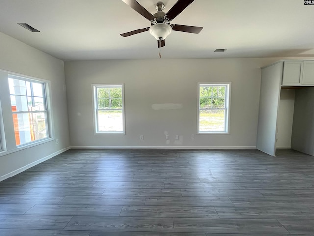 spare room with baseboards, dark wood-type flooring, visible vents, and a healthy amount of sunlight