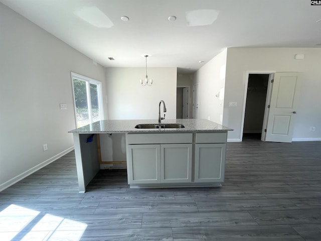 kitchen with dark wood finished floors, a sink, an island with sink, light stone countertops, and baseboards