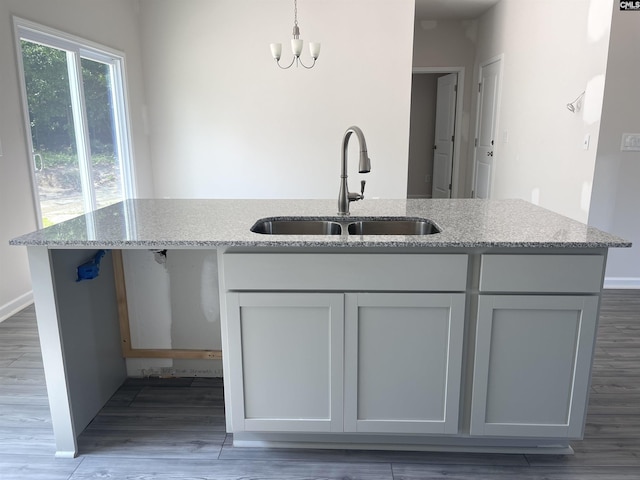 kitchen with hanging light fixtures, wood finished floors, a sink, and light stone countertops