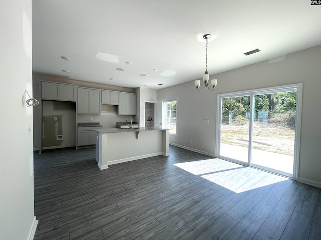 kitchen with a chandelier, dark wood-type flooring, a sink, baseboards, and a center island with sink