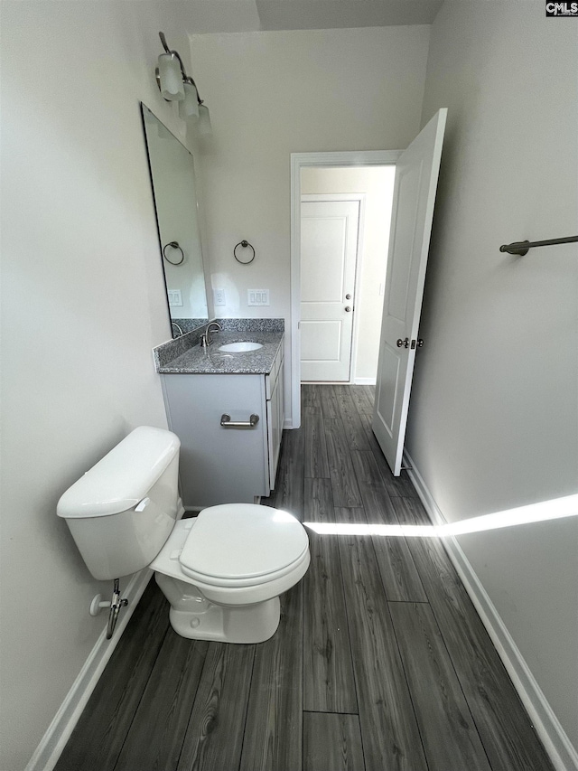 half bathroom with vanity, wood finished floors, toilet, and baseboards