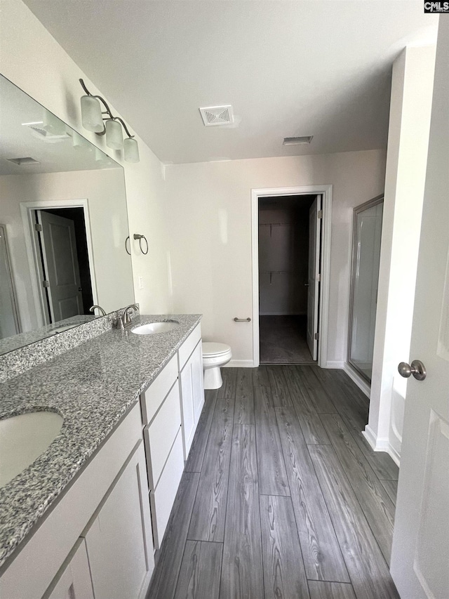 bathroom with a stall shower, visible vents, toilet, wood finished floors, and a sink