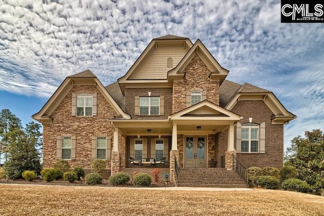 craftsman-style house with stone siding, french doors, a porch, and brick siding