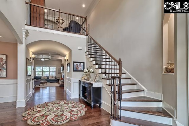 foyer entrance featuring arched walkways, a decorative wall, a high ceiling, ceiling fan, and wood finished floors