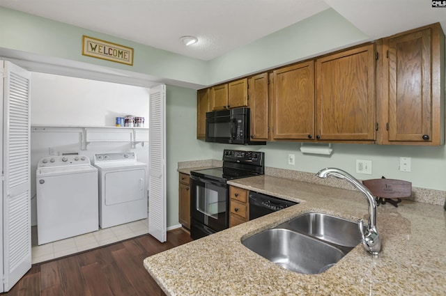 kitchen featuring separate washer and dryer, dark wood-type flooring, a sink, black appliances, and brown cabinetry