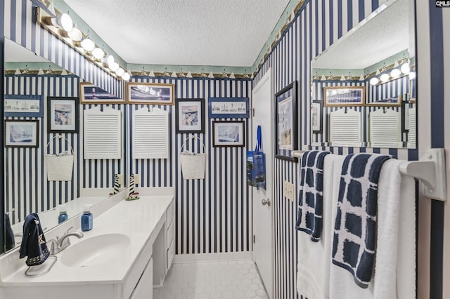 bathroom featuring tile patterned floors, a sink, a textured ceiling, and wallpapered walls