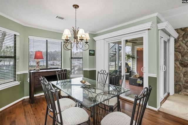 dining area featuring dark wood-style flooring, crown molding, a notable chandelier, visible vents, and baseboards