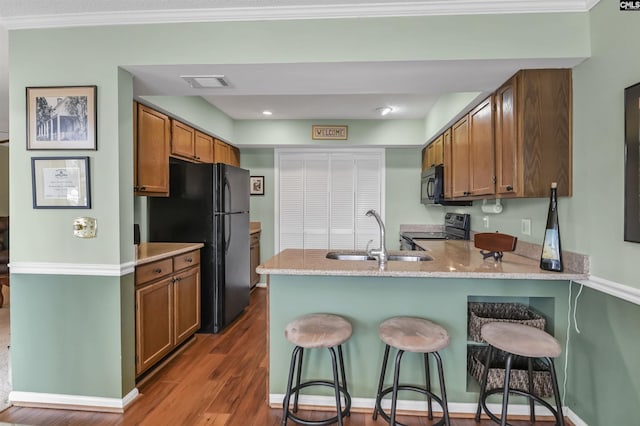 kitchen featuring visible vents, wood finished floors, a peninsula, black appliances, and a sink