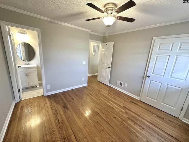 unfurnished bedroom with baseboards, visible vents, wood finished floors, crown molding, and a textured ceiling