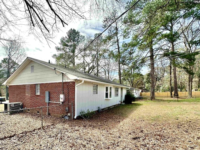 view of side of home with brick siding, fence, and central AC unit