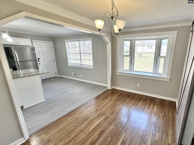 unfurnished dining area featuring ornamental molding, a textured ceiling, wood finished floors, a chandelier, and baseboards