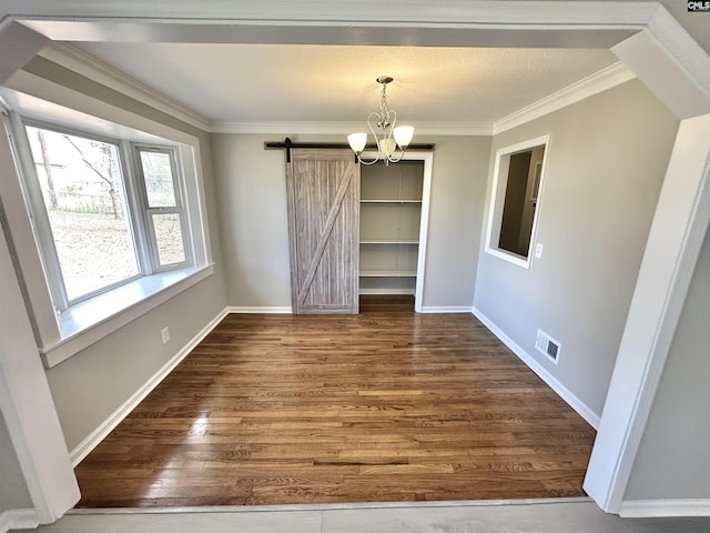 unfurnished dining area with a barn door, visible vents, wood finished floors, an inviting chandelier, and crown molding