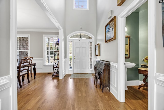 foyer entrance featuring a wainscoted wall, crown molding, and wood finished floors