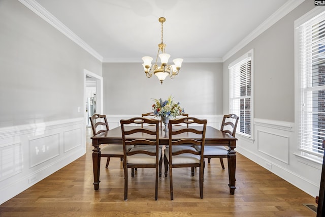 dining space with an inviting chandelier, crown molding, wood finished floors, and wainscoting