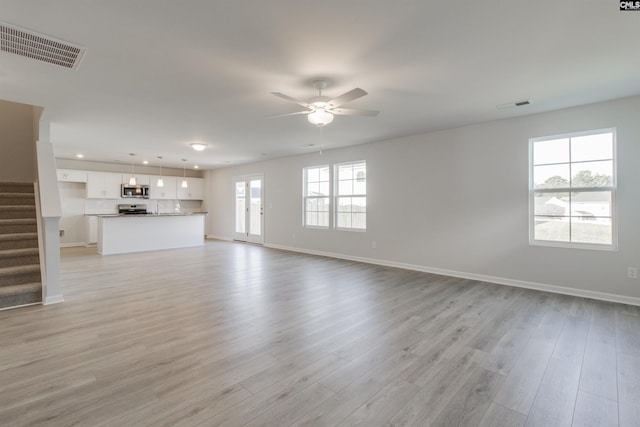 unfurnished living room with stairway, a ceiling fan, visible vents, and light wood-style floors