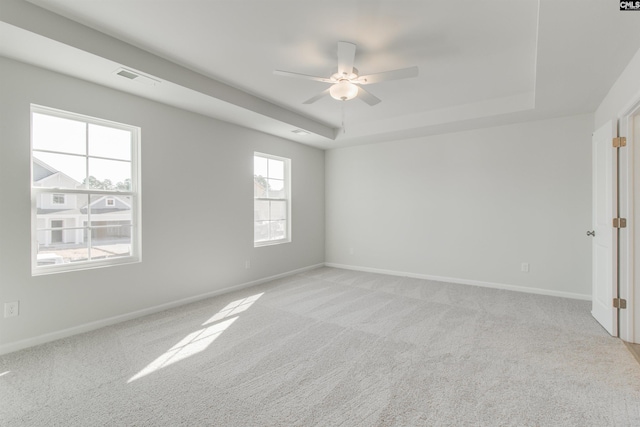 unfurnished room with visible vents, a tray ceiling, light colored carpet, and baseboards