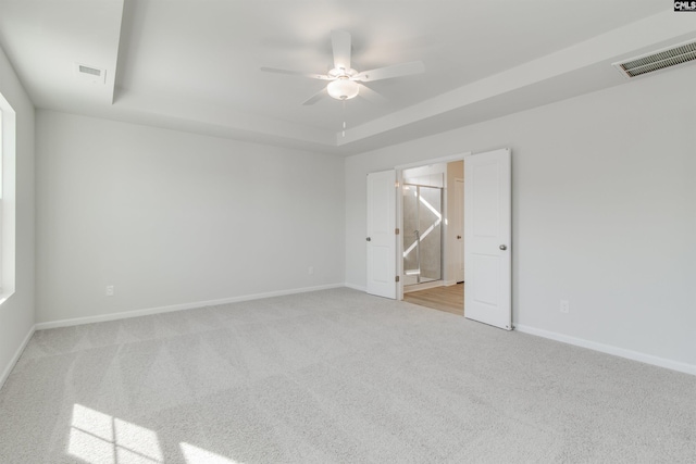 carpeted empty room featuring a tray ceiling, a ceiling fan, visible vents, and baseboards