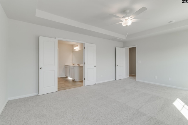 unfurnished bedroom featuring ensuite bath, baseboards, a raised ceiling, and light colored carpet