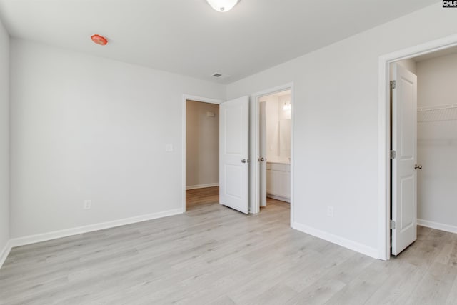 unfurnished bedroom featuring light wood finished floors, visible vents, baseboards, a walk in closet, and a closet