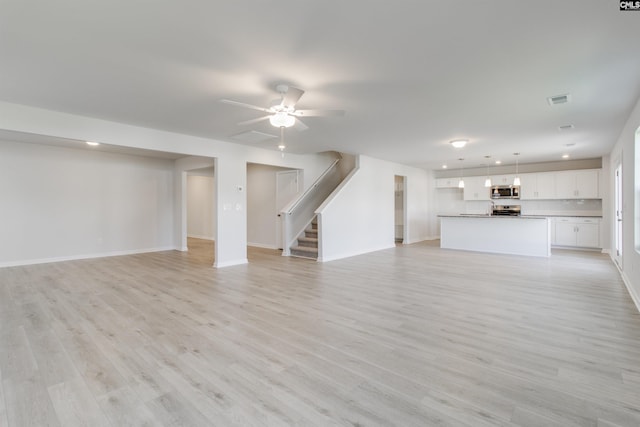 unfurnished living room featuring light wood finished floors, visible vents, ceiling fan, baseboards, and stairs