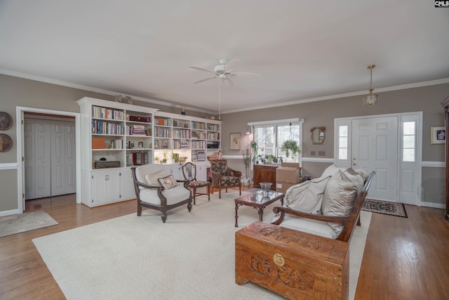 living room featuring a ceiling fan, crown molding, baseboards, and wood finished floors