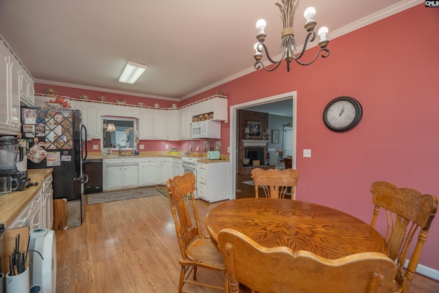 dining area featuring light wood-type flooring, an inviting chandelier, a brick fireplace, and crown molding