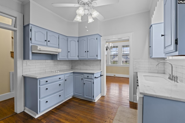 kitchen featuring dark wood-style flooring, ornamental molding, a sink, under cabinet range hood, and baseboards