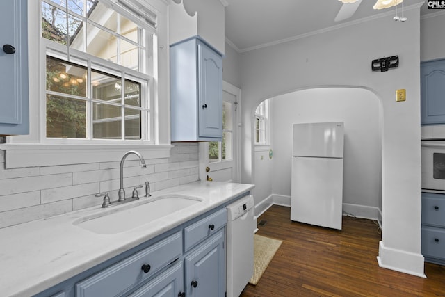 kitchen featuring crown molding, blue cabinetry, tasteful backsplash, a sink, and white appliances