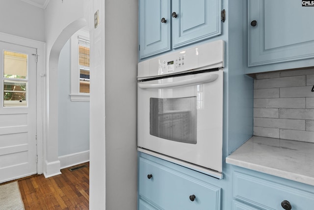 kitchen with arched walkways, visible vents, baseboards, blue cabinetry, and dark wood finished floors