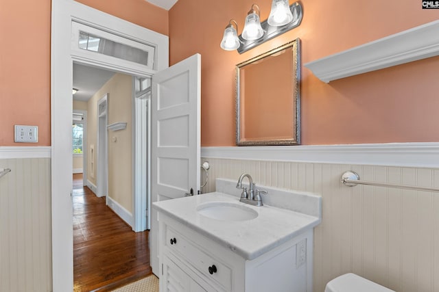 half bathroom featuring toilet, a wainscoted wall, wood finished floors, and vanity