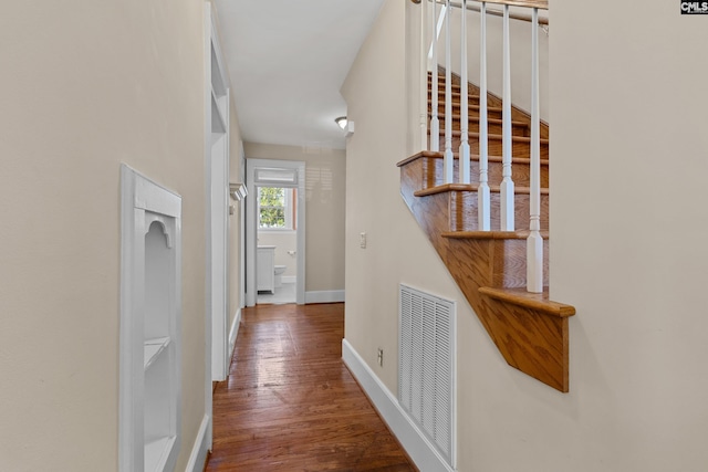 corridor with stairs, visible vents, baseboards, and wood finished floors