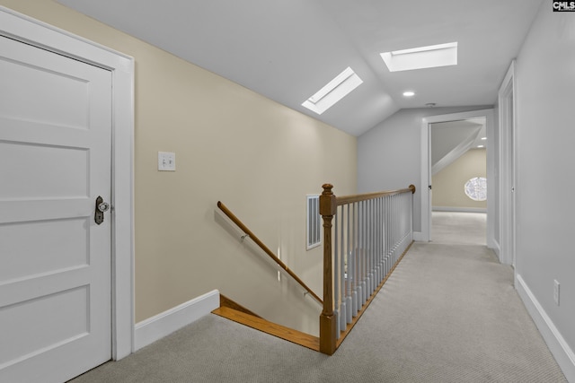 corridor featuring vaulted ceiling with skylight, visible vents, an upstairs landing, baseboards, and carpet