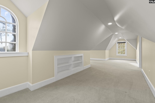 bonus room featuring built in shelves, carpet, vaulted ceiling, and baseboards