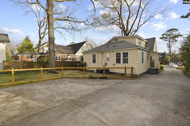 rear view of house with a fenced front yard, entry steps, and a shingled roof