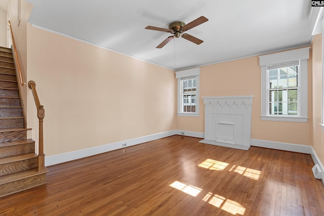 unfurnished living room featuring hardwood / wood-style floors, stairway, a fireplace with flush hearth, and a wealth of natural light