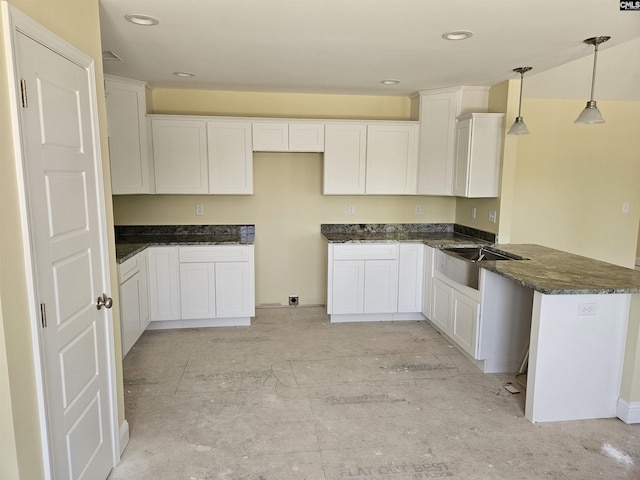 kitchen with white cabinets, dark stone counters, decorative light fixtures, a peninsula, and a sink