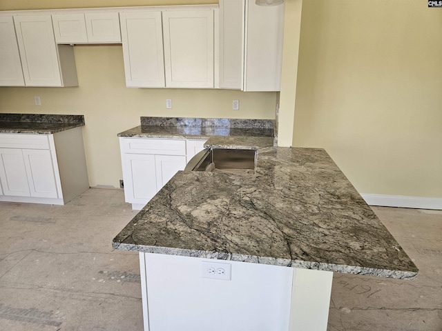 kitchen with baseboards, a peninsula, dark stone countertops, and white cabinets