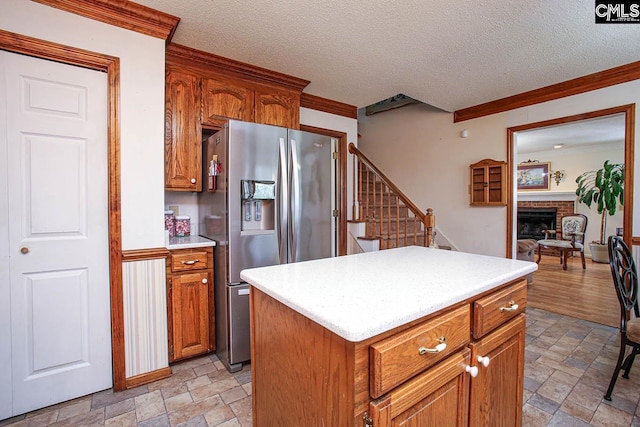 kitchen featuring stone tile floors, crown molding, stainless steel refrigerator with ice dispenser, and light countertops