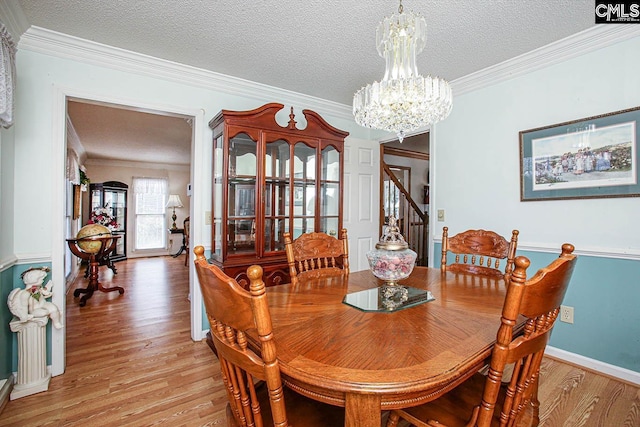 dining space with a chandelier, light wood-type flooring, crown molding, and a textured ceiling