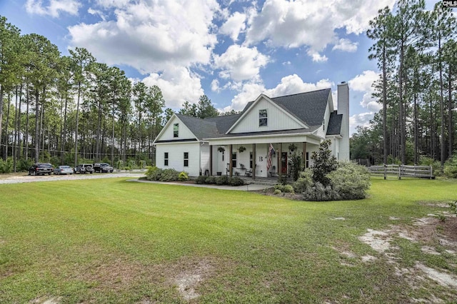 modern farmhouse with a porch, a chimney, a front yard, and fence