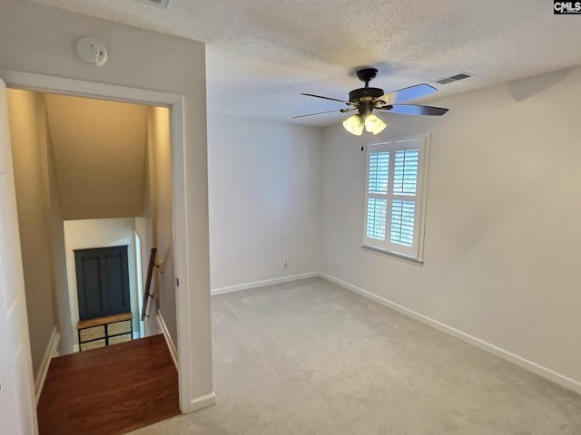 unfurnished living room featuring a textured ceiling, light colored carpet, a ceiling fan, baseboards, and visible vents