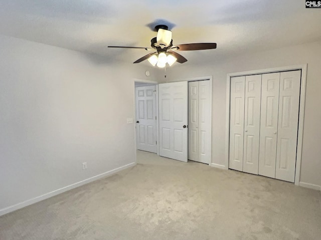 unfurnished bedroom featuring multiple closets, light colored carpet, ceiling fan, and baseboards