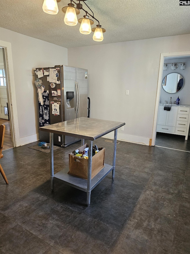 kitchen with a sink, baseboards, a textured ceiling, and stainless steel fridge with ice dispenser