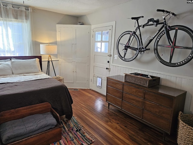 bedroom with a wainscoted wall, a textured ceiling, and dark wood finished floors