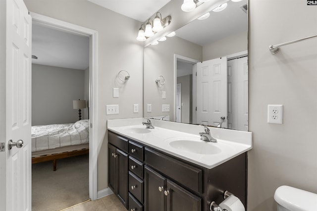 ensuite bathroom with double vanity, tile patterned flooring, toilet, and a sink