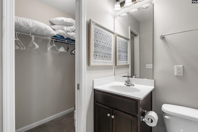 bathroom featuring vanity, a spacious closet, toilet, and baseboards