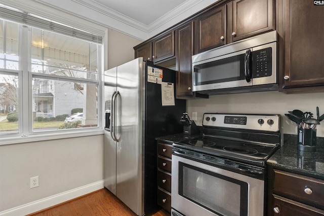 kitchen with dark stone countertops, wood finished floors, ornamental molding, dark brown cabinets, and appliances with stainless steel finishes