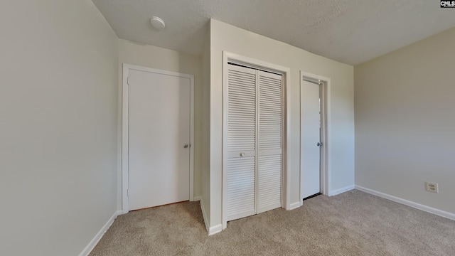 unfurnished bedroom with baseboards, a closet, a textured ceiling, and light colored carpet